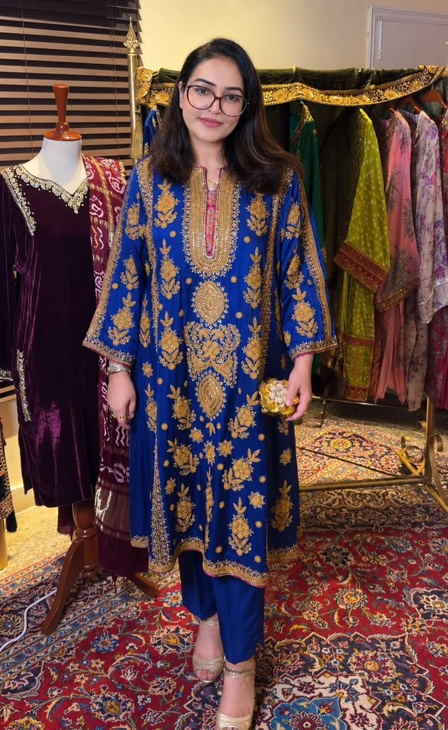 Woman in glasses wearing a royal blue kurta with gold embroidery in a boutique with garments on racks