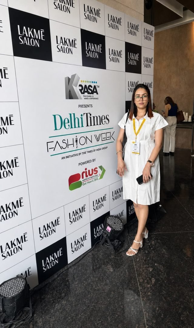 Woman in a white shirt dress standing in front of the Delhi Times Fashion Week backdrop