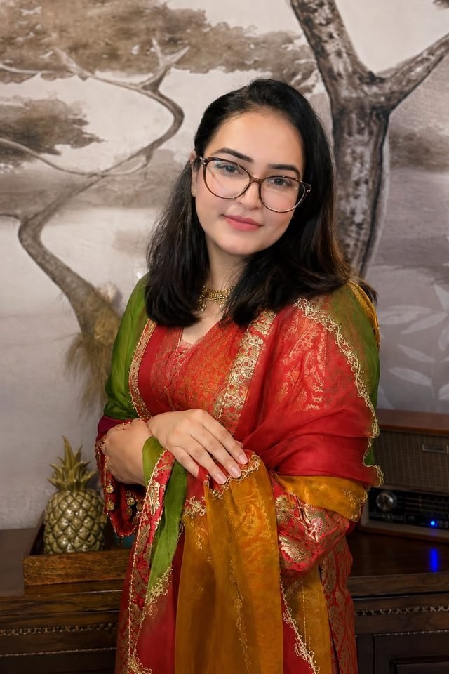 Woman in glasses wearing a red and gold brocade kurta with a green and mustard organza dupatta
